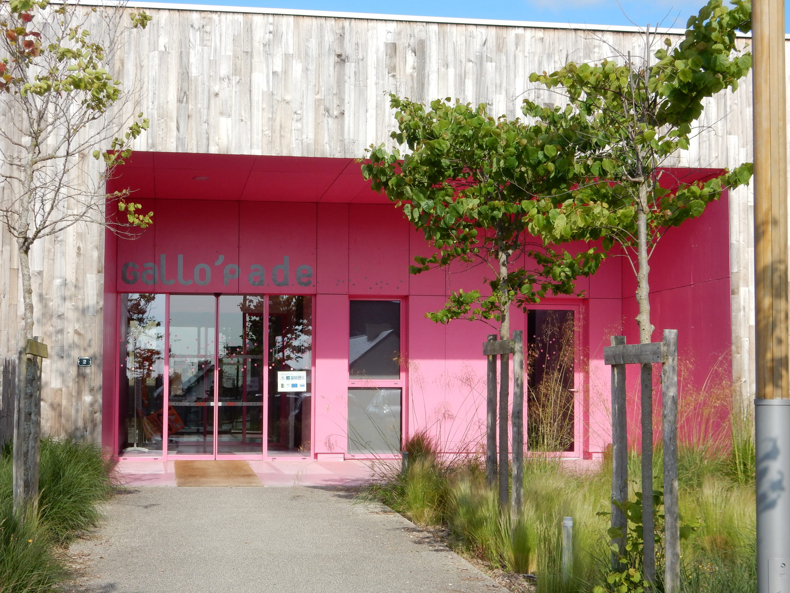 maison de l'enfance gallo'pade bâtiment rose et en bois naturel avec des arbres à l'entrée