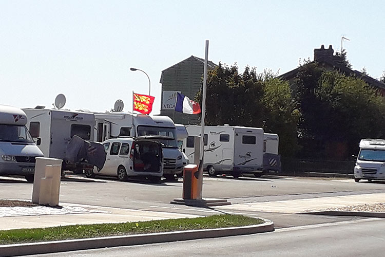 aire de camping car avec véhicules stationnés et des drapeaux
