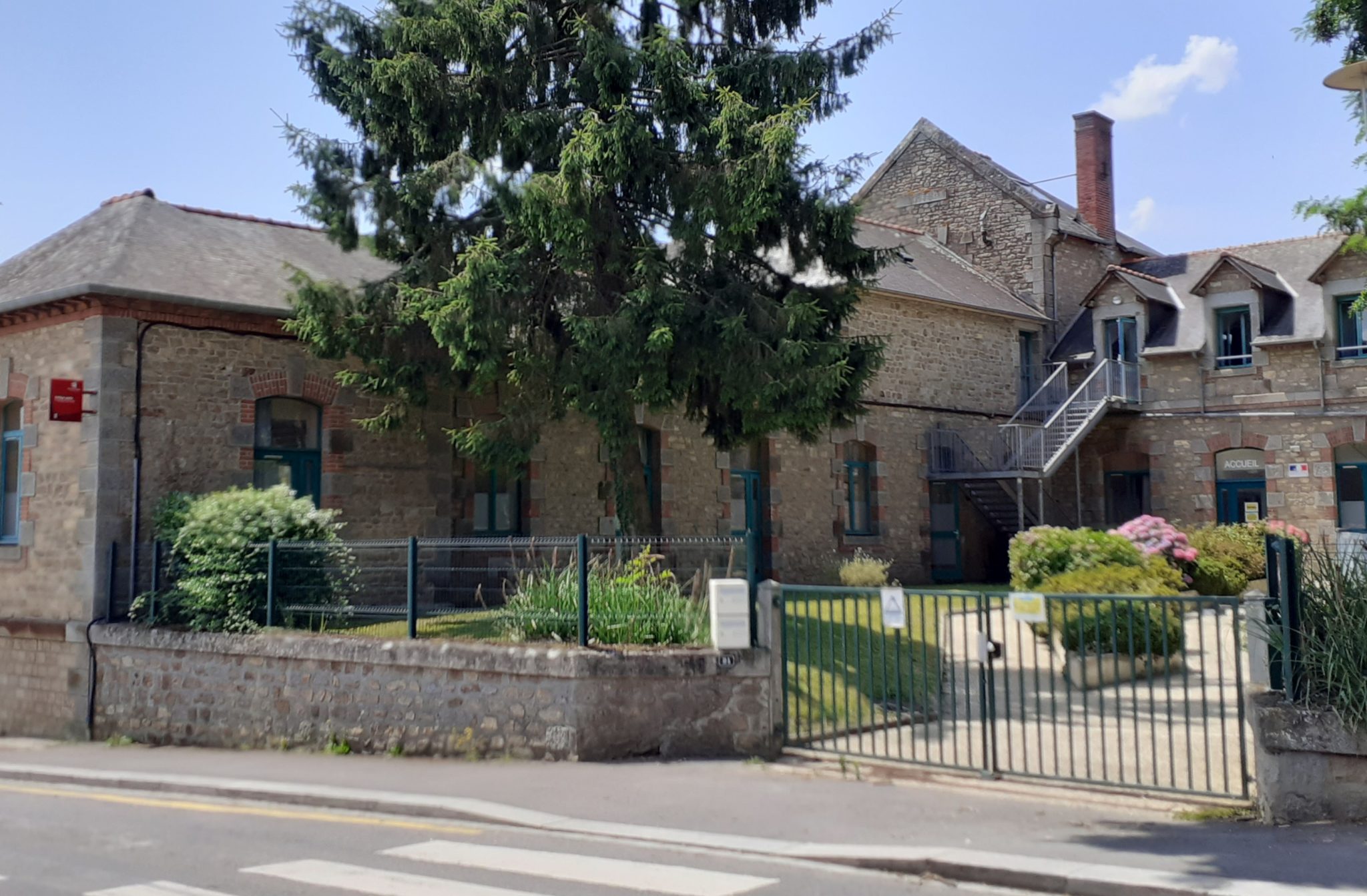 collège public françois brune avec des bâtiments en pierre des ouvertures vertes et au premier plan de la végétation arbres et fleurs